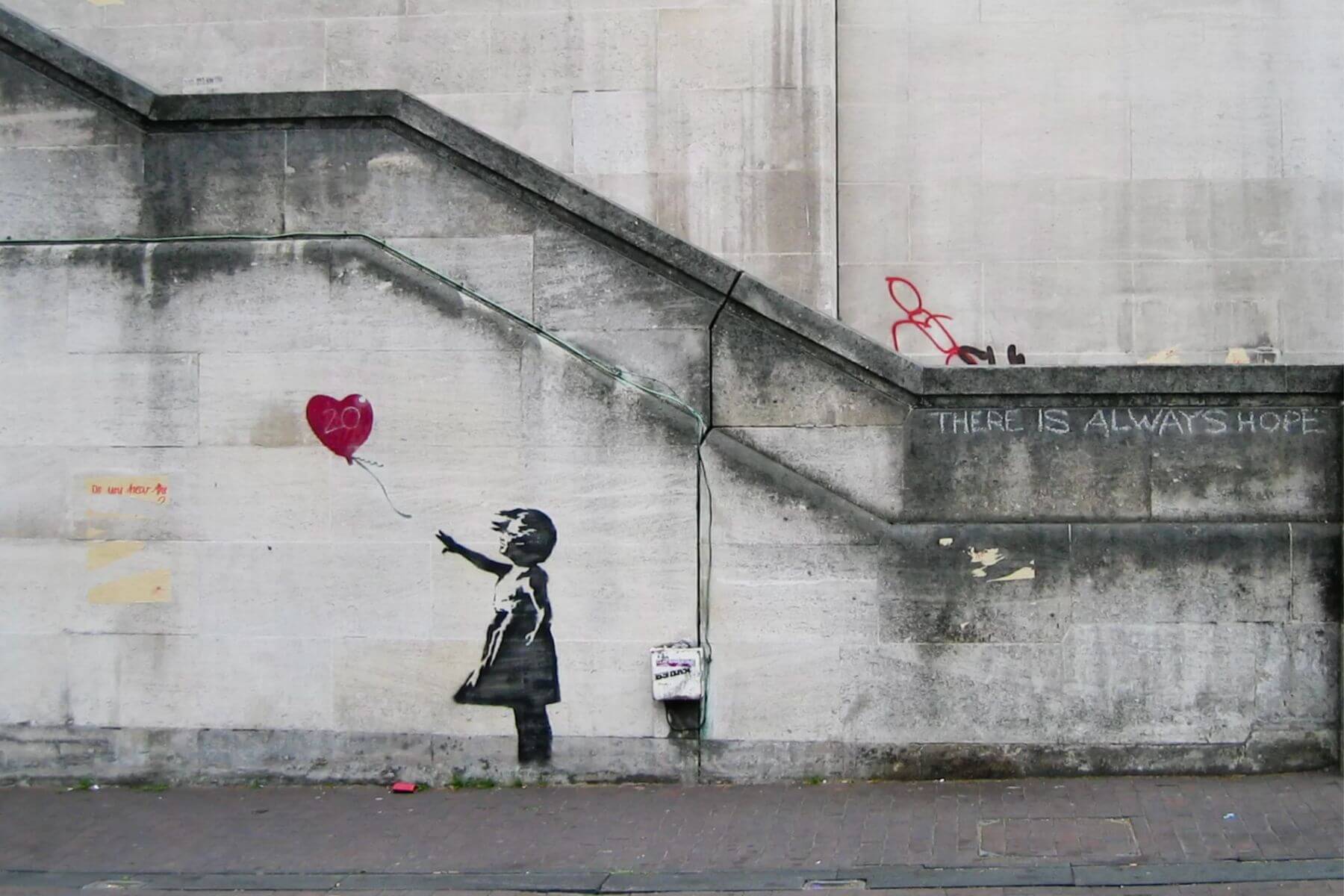 A young girl reaching toward a red heart-shaped balloon floating away