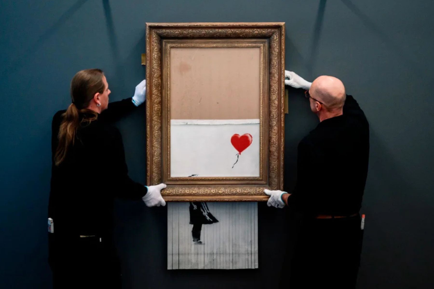 banksy-love-is-in-the-bin-2018-the-lawless-muse A partially shredded framed artwork hanging on a gallery wall