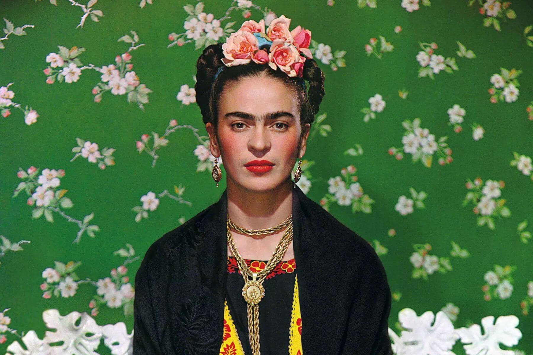 kahlo-portrait-green-wallpaper-the-lawless-muse Frida Kahlo posed in front of a green floral wallpaper wearing bold jewelry and flowers in her hair