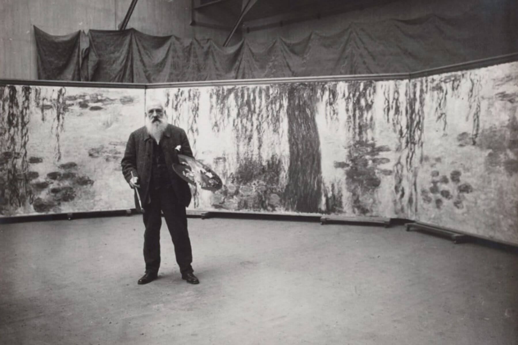 Claude Monet standing with his palette in front of a large canvas of water lilies